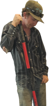 A person in a patterned shirt and baseball cap holds a long red-handled tool, standing against a black background.